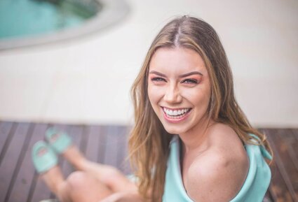 blond woman sitting by pool smiling nice white teeth after dental veneers Beverly Grove, Los Angeles, CA cosmetic dentist